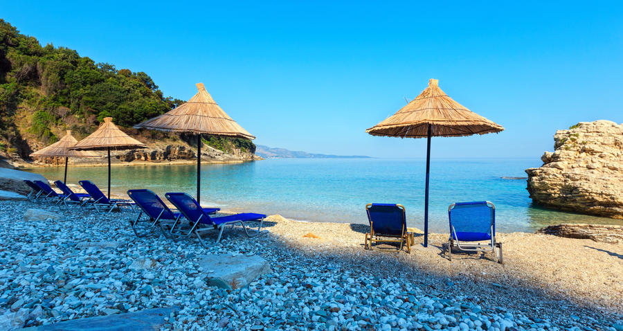 Summer morning Pulebardha beach with sunbeds, strawy sunshades and pebble (Saranda, Albania).