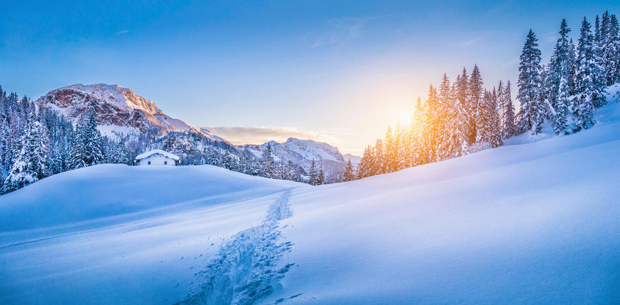 Panoramic view of beautiful winter wonderland mountain scenery with traditional mountain cabin the background in the Alps in golden evening light at sunset