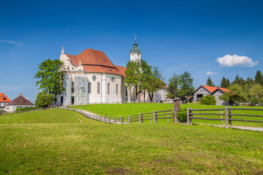 Beautiful view of famous oval rococo Pilgrimage Church of Wies (Wieskirche), a UNESCO World Heritage Site since 1983, with green meadows on a sunny day with blue sky and clouds in Bavaria, Germany