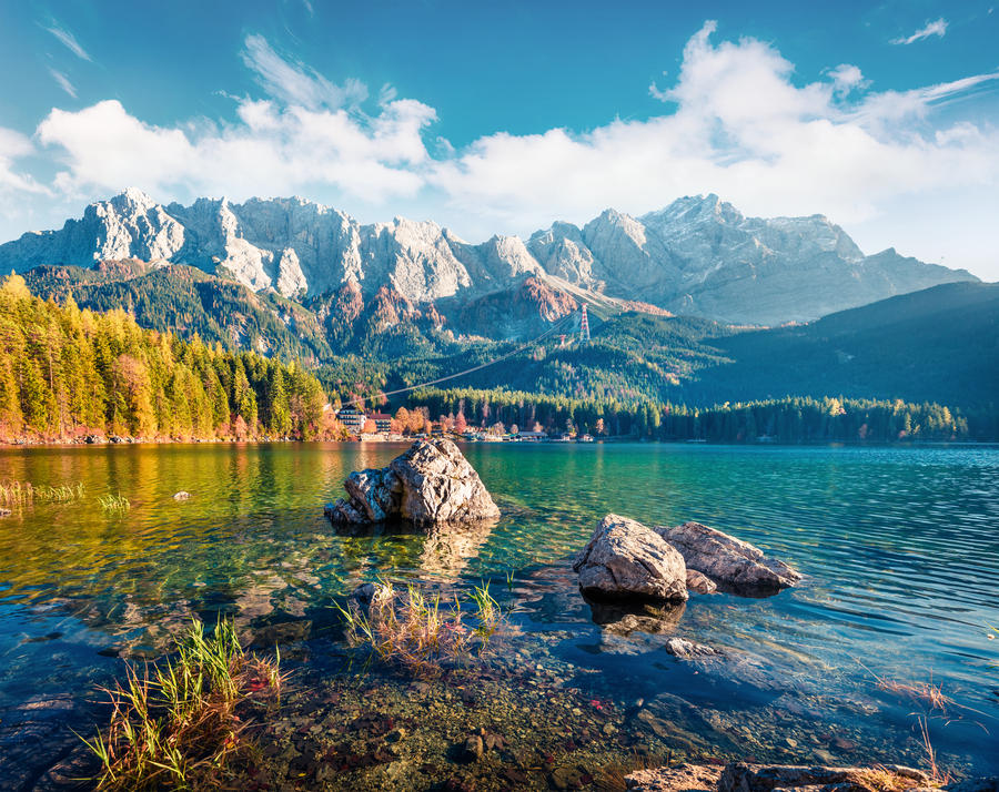 Sunny evening scene of Eibsee lake with Zugspitze mountain range on background. Colorful autumn view of Bavarian Alps, Germany, Europe. Beauty of nature concept background.