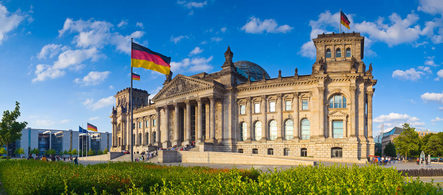 Warm evening sunlight illuminating the mighty Reichstag parliament (1894) with clear blue sky and flags flying.