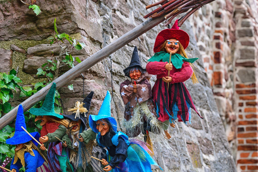 Many multicolored figurines of witches hanging on a broom in front of a medieval wall, in wernigerode, harz, germany.