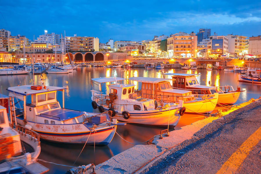 Old harbour of Heraklion with fishing boats and marina during twilight blue hour, Crete, Greece. Boats blurred motion on the foreground.