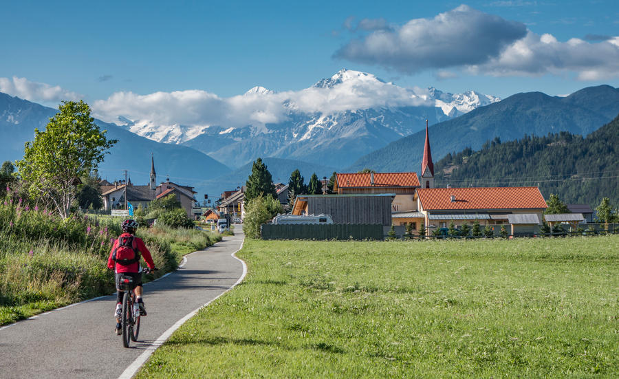 senior woman under way with her e-bike on the famous bicycle route Via Claudia Augusta, Alto adige,Italy, Mount Ortler in the background