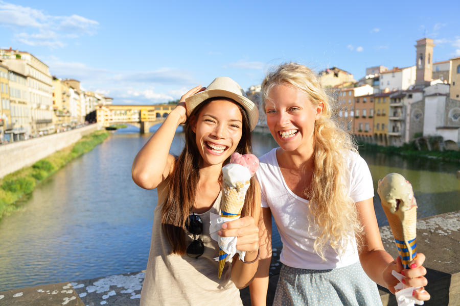 Happy women friends eating ice cream on travel in Florence. Cheerful girlfriends enjoying italian food gelato cone smiling happy by Ponte Vecchio during vacation holidays in Tuscany, Italy, Europe.