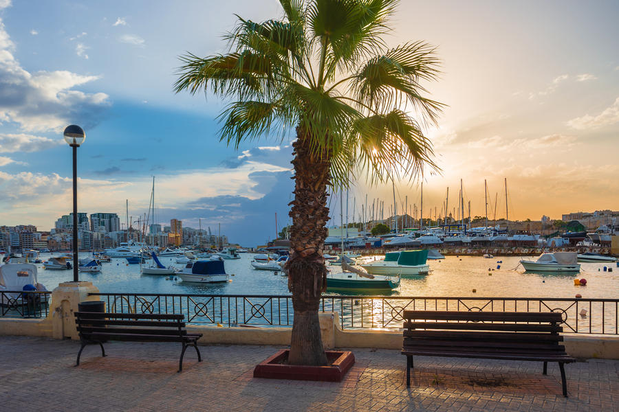 Beautiful sunrise with benches, palm tree and sailboats at Sliema bay, Malta