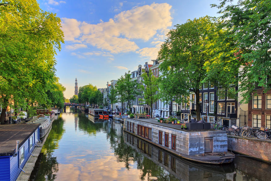 Houseboats at the UNESCO world heritage Prinsengracht canal with the Westerkerk (Western church) on a summer morning with a blue sky and clouds and a mirror reflection in Amsterdam, The Netherlands