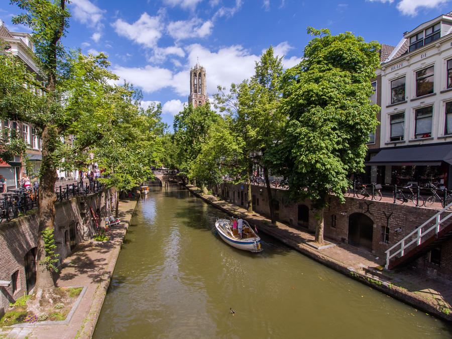 Boat sailing in the Oudegracht canal in Utrecht, Holland on a sunny day with the 'Dom' church tower in the background
