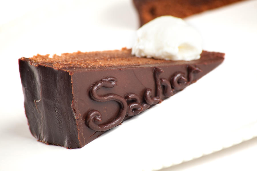 A photo of the Austrian Sacher Torte cake, filled with apricot preserve and frosted with darl chocolate with a dollop of whipped cream. Isolated on white