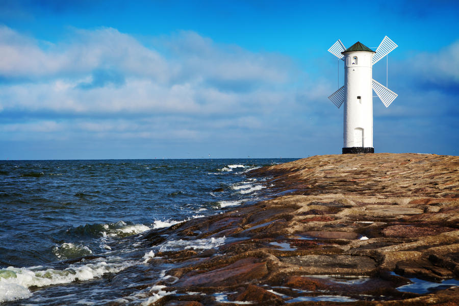 White old lighthouse in Swinoujscie, stone pier and wavy sea, Poland