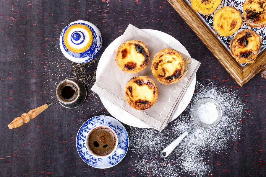 Traditional Portugese pastry Pastel de Nata served with coffee and honey on traditional tray over a rustic wooden board. Top View.