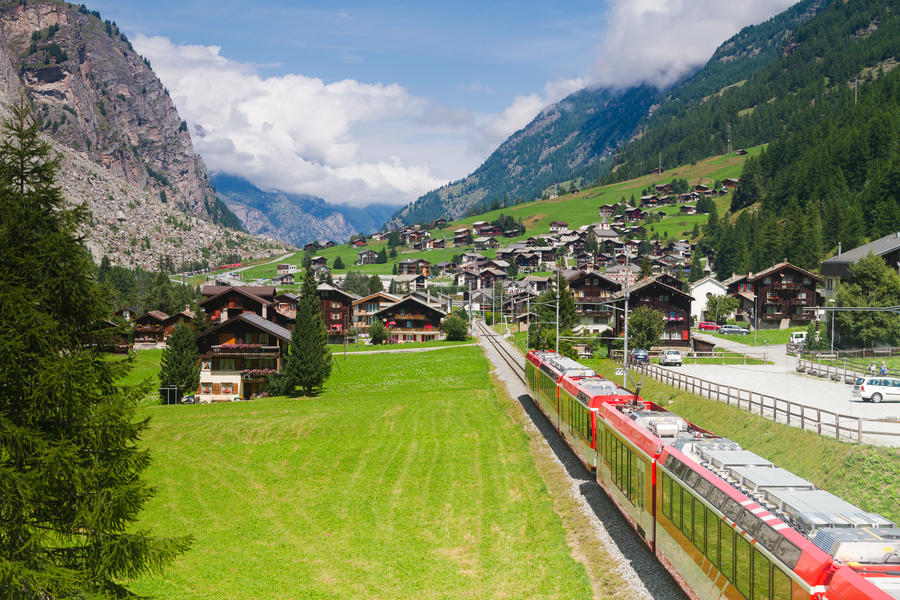 Red (glacier express) train heading through high mountain valley in switzerland alps on route from St. Moritz to Zermatt.
