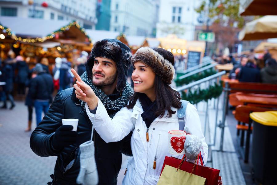 Happy young couple shopping on the street at christmas market, smiling, drinking hot drinks.