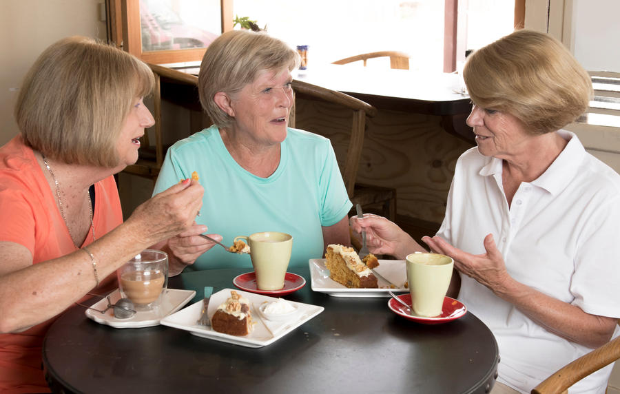 group of three lovely middle age senior mature women girlfriends meeting for coffee and tea with cakes at coffee shop sharing time together enjoying converstion happy and cheerful gossiping