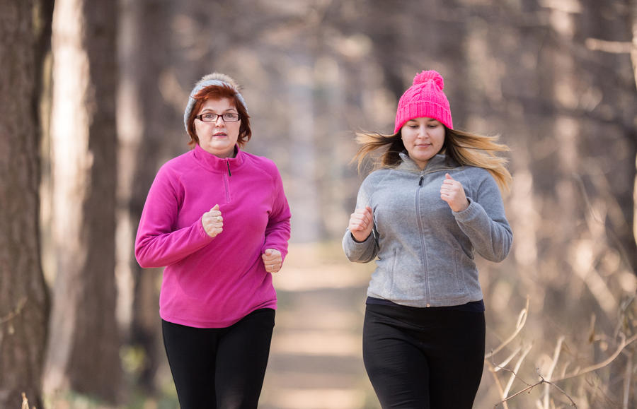 Mother and daughter wearing sportswear and running in forest at mountain during winter