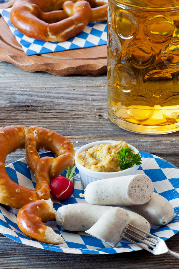 Blue-white paper plate with Veal sausage, pretzel, mustard and radish and a glass with beer on an old rustic wooden table