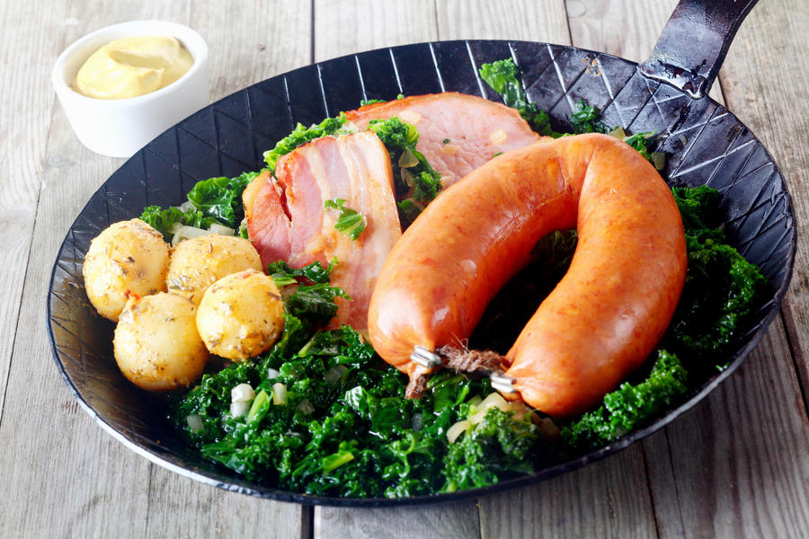 Close up Freshly Cooked Potatoes, Kassler and Sausage with Kale Veggies on Frying Pan with Dipping Sauce on Side.