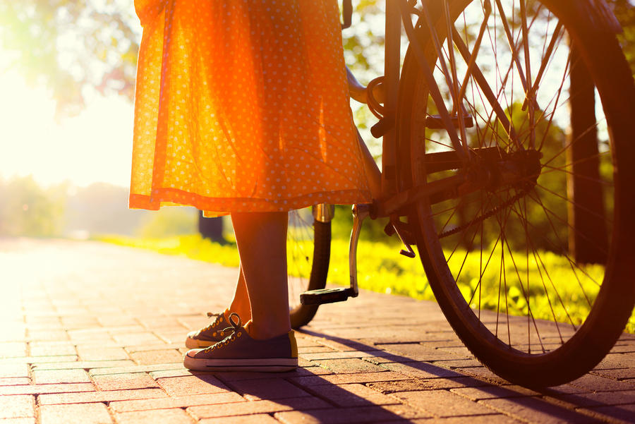 Girls legs and long vintage orange skirt. Close up photo of girl stand with her bicycle in the city park at the sunset.
