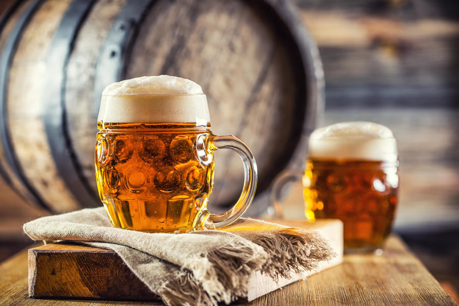 Two glasses full of beer with wooden barel.