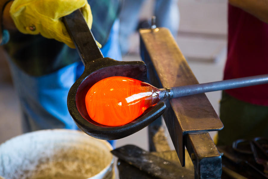 A very talented glassblower is forming and shaping glass in a studio for glass making. He is creating a fluted bowl from this piece of molten glass.