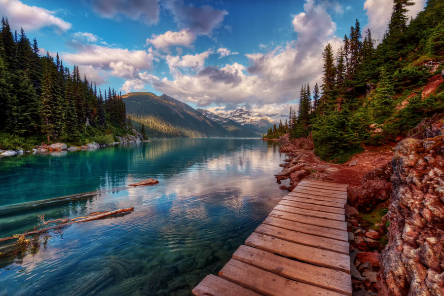 Wooden walkway along clear mountain lake and evergreen trees