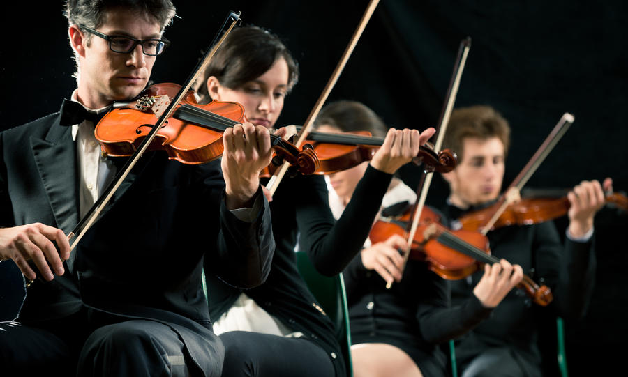 Violin orchestra performing on stage on dark background.