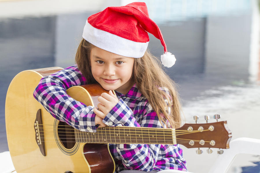 Girl with brown straw hat playing acoustic guitar near pool