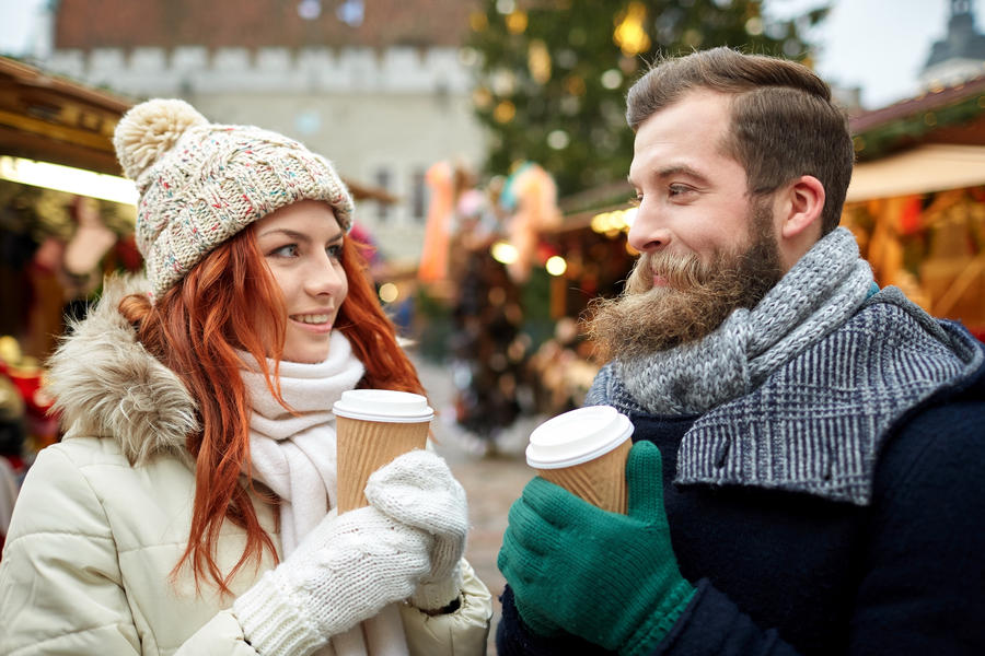 holidays, winter, christmas, hot drinks and people concept - happy couple of tourists in warm clothes drinking coffee from disposable paper cups in old town