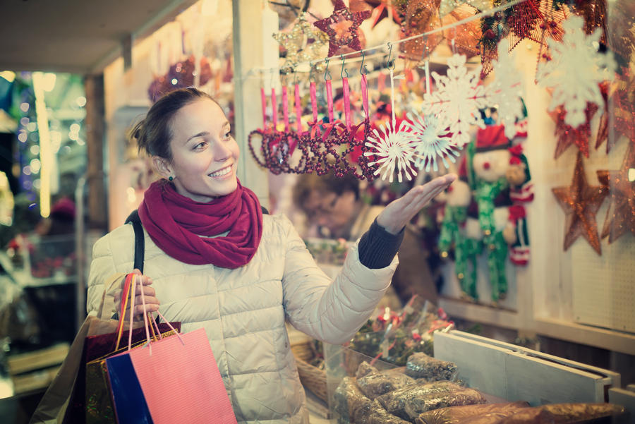 Happy smiling young brunette choosing gifts and decorations at Christmas fair in evening