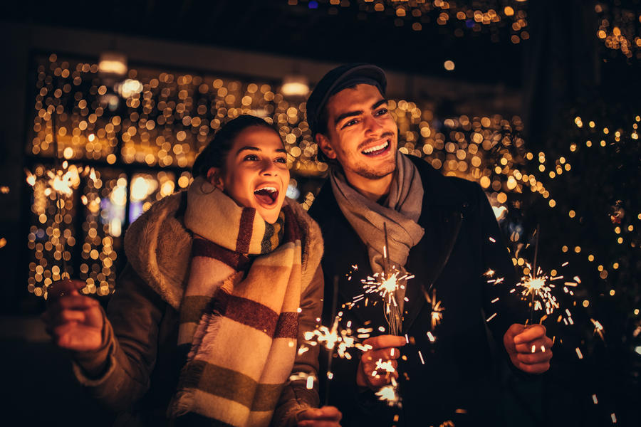 Cheerful couple playing with sparklers at Christmas night outdoors