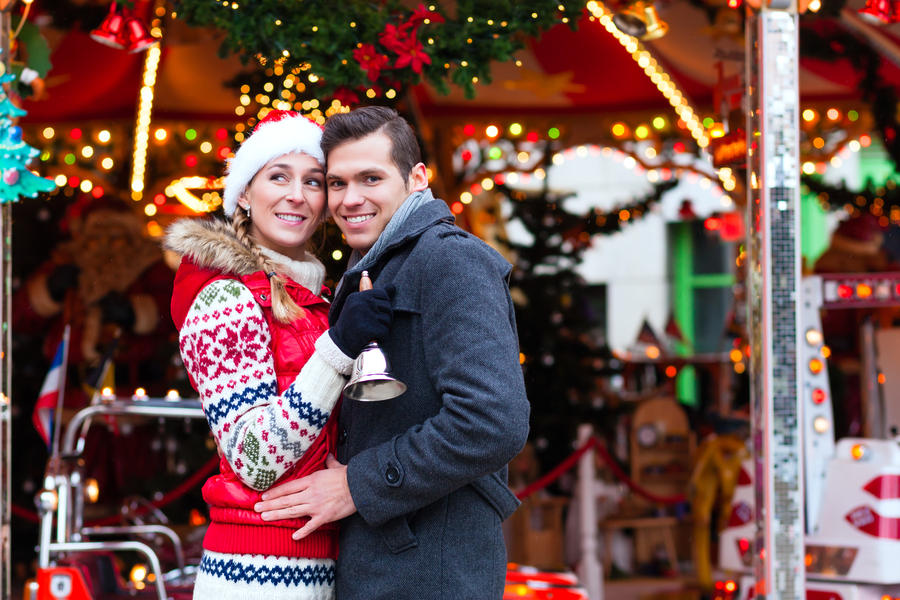 Man and woman or  a couple  or friends during advent season or holiday in front of a carousel or &quot;marry-go-round&quot; on the Christmas or Xmas market