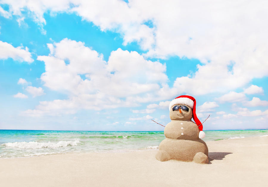 Smiling sandy snowman in red santa hat on sea beach. New Years and Christmas holidays in hot countries concept