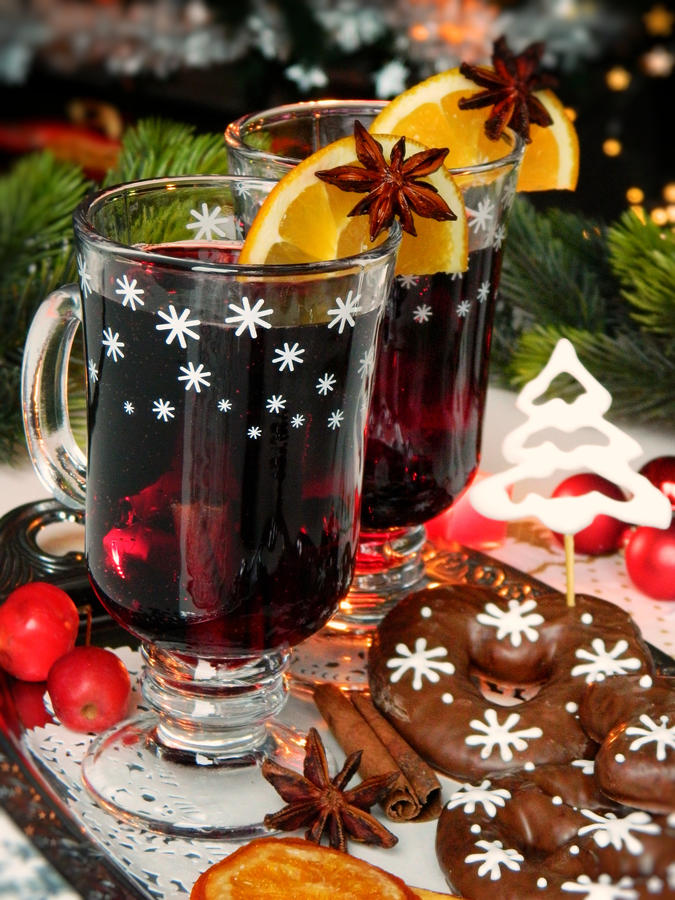 Two glasses with mulled wine on a tray with chocolate gingerbread on a Christmas tree background.