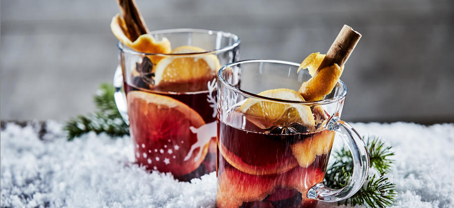 Panorama banner with two glasses of Christmas Gluhwein or mulled red wine garnished with stick cinnamon and served on winter snow with copy space