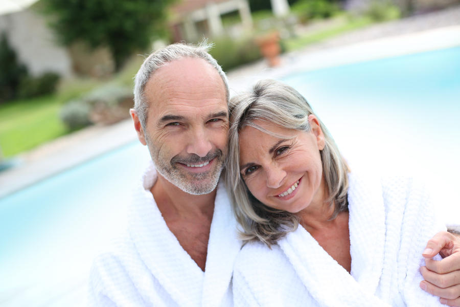 Happy senior couple in bathrobe by resort pool