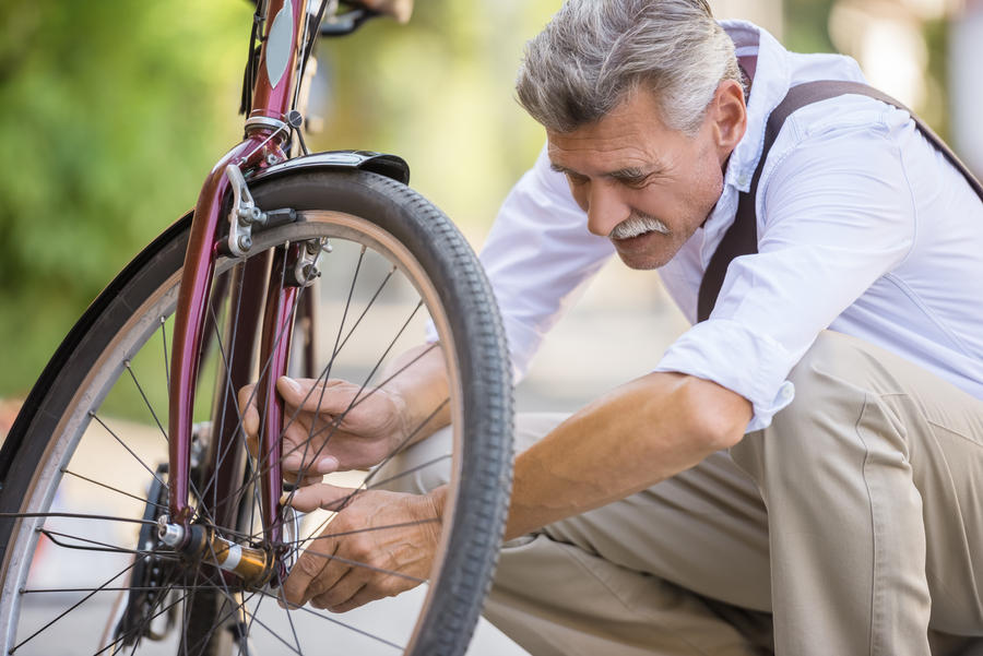 Senior man is repairing bike in the street.