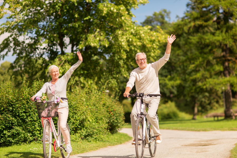 active old age, people and lifestyle concept - happy senior couple riding bicycles and waving hand at summer park