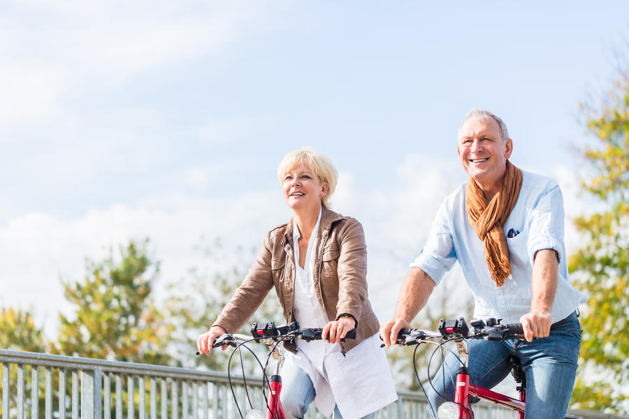 Senior couple, married woman and man, riding their bicycles over a bridge enjoying some leisure time