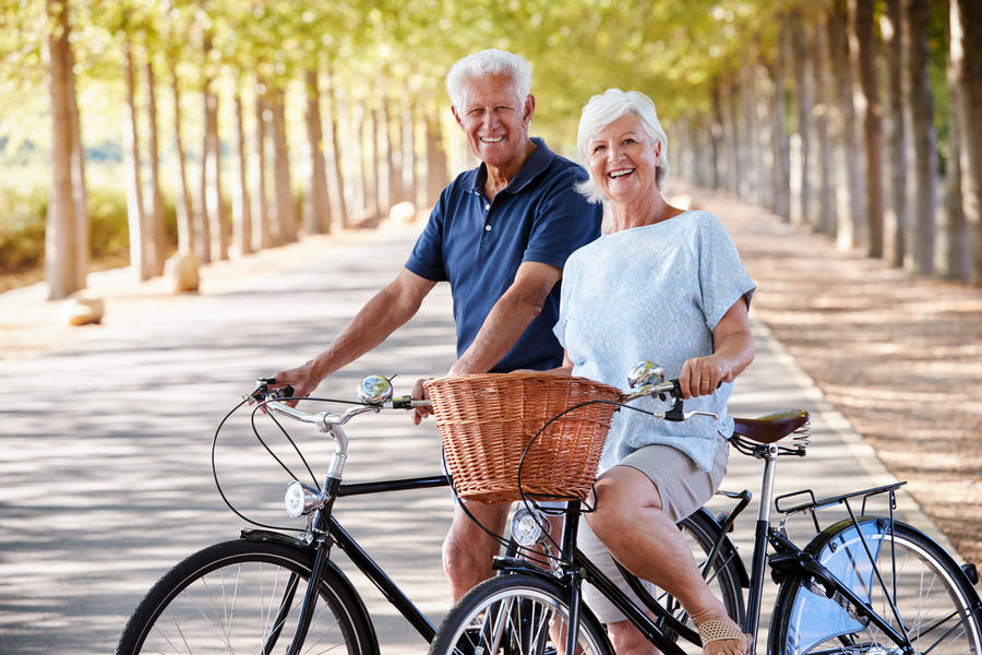 Portrait Of Smiling Senior Couple Cycling On Country Road