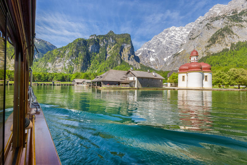 Classic view of traditional passenger boat on Lake Konigssee with famous Sankt Bartholomae pilgrimage church and Watzmann on a beautiful sunny day in summer, Berchtesgadener Land, Bavaria, Germany