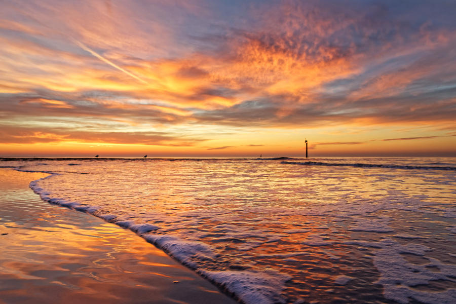 Sunset on the beach of Norderney, Germany, with a wave and foam in the foreground