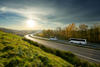 White buses traveling on the highway turning towards the horizon in an autumn landscape at sunset