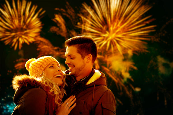 Young couple in love celebrating Christmas with fireworks outdoors.