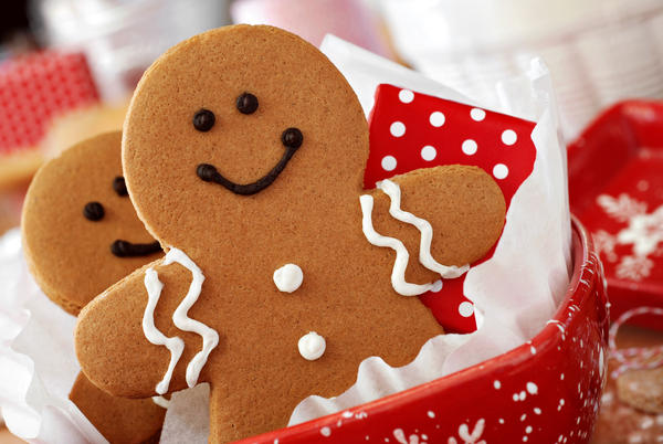 Smiling gingerbread men nestled in holiday dish with gift-wrapped surprise.  Baking ingredients and supplies (including baker&#39;s twine and rolling pin) in background.  Macro with extremely shallow dof.