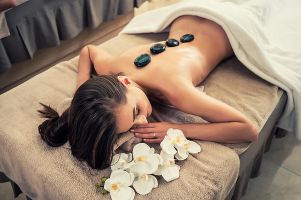 High angle view of young woman lying down on massage bed with traditional hot stones along the spine at spa and wellness center