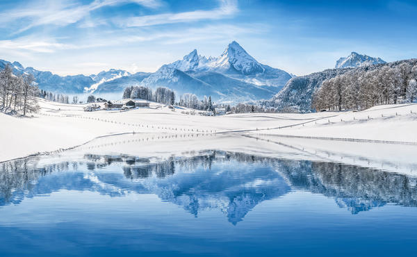 Panoramic view of beautiful white winter wonderland scenery in the Alps with snowy mountain summits reflecting in crystal clear mountain lake on a cold sunny day with blue sky and clouds