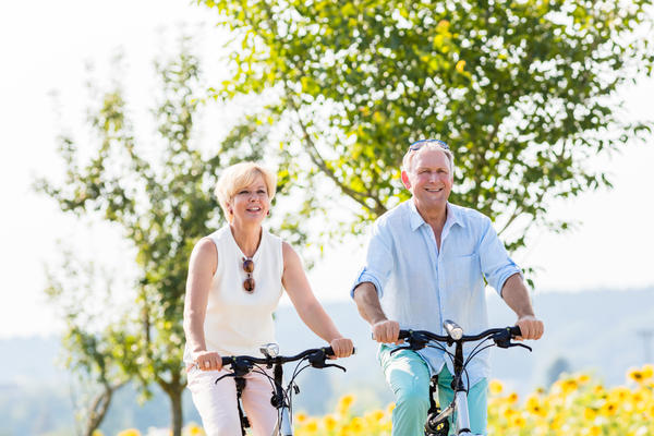 Senior couple, woman and man, riding their bikes along field of sunflowers